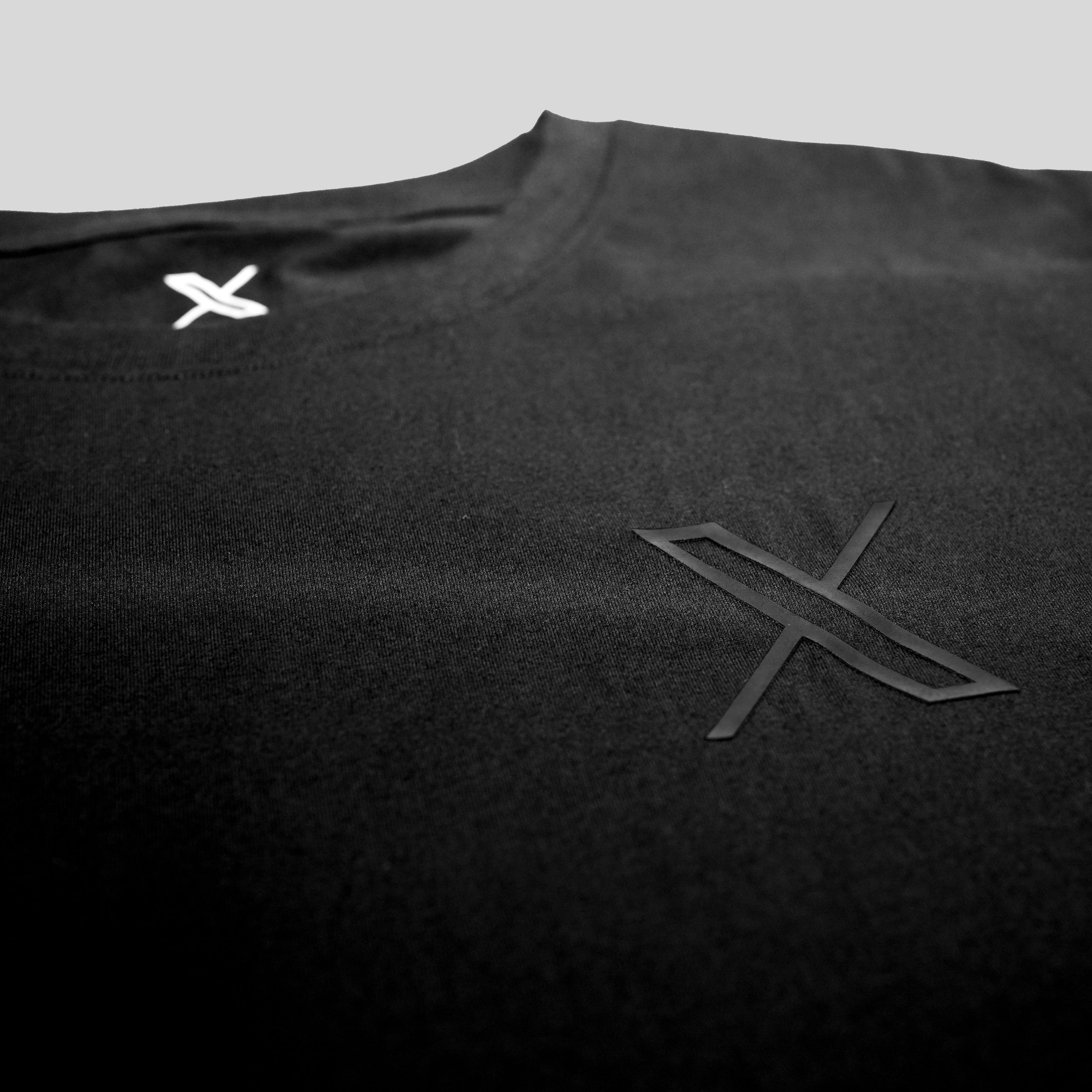 A closeup of the Unisex 3D Logo Tee showing the collar and chest area of a black shirt with a small X logo in black on the left chest.