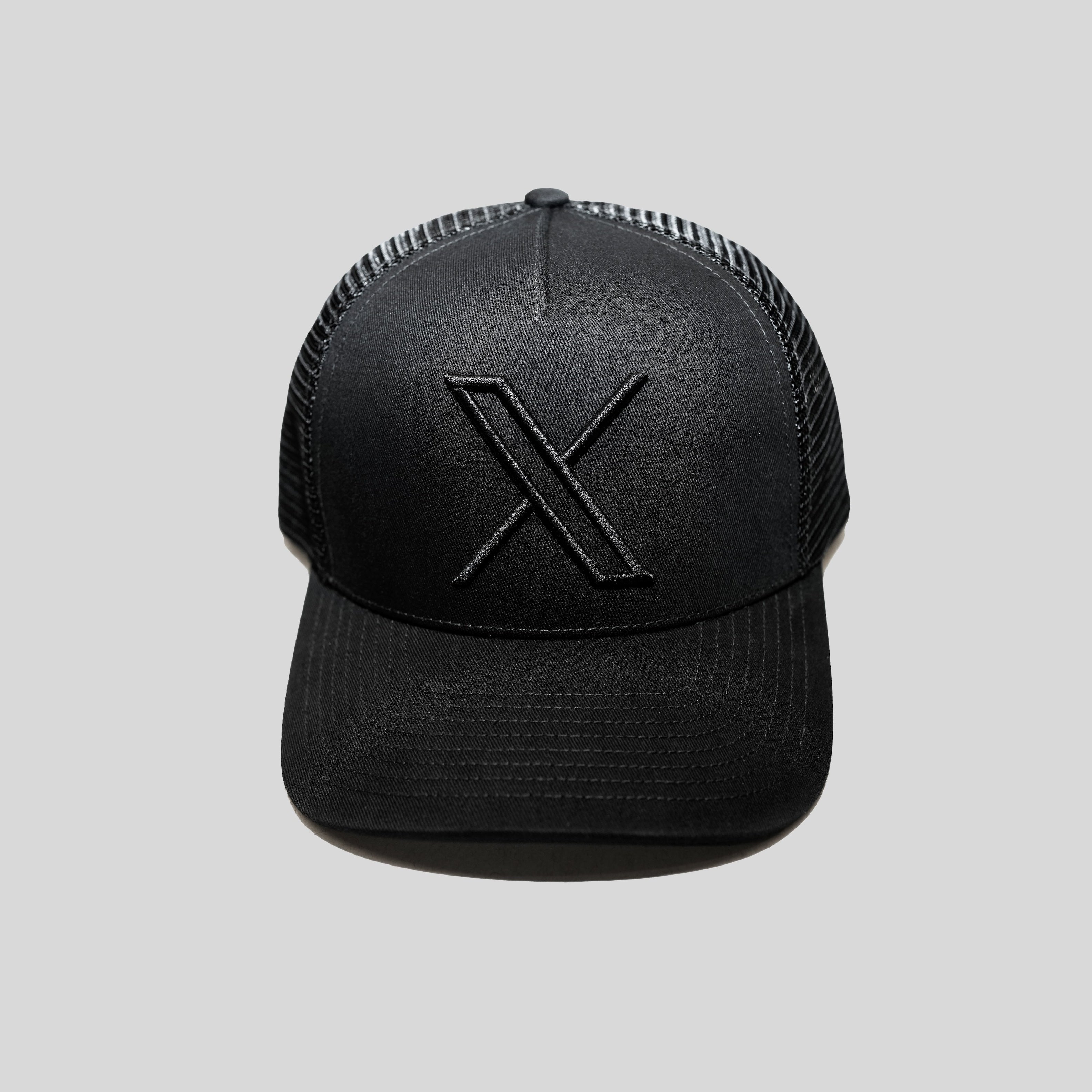 An image of the Unisex 3D Logo Trucker Hat, a black hat shown from the front with an embroidered X logo in black on the front.