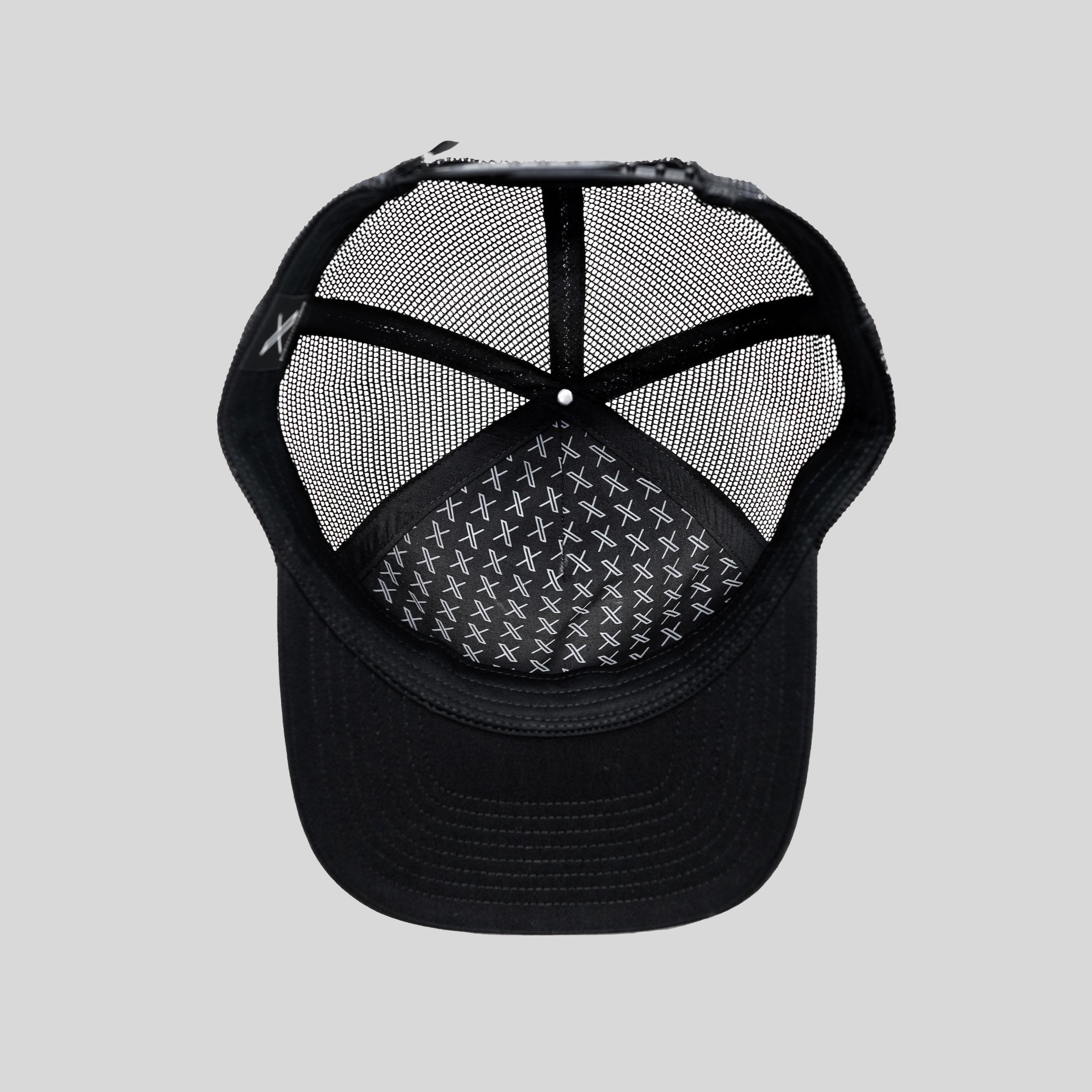 An image of the Unisex 3D Logo Trucker Hat showing the full underside of the black hat, with a black mesh back and white X logo pattern printed on the inside fabric.