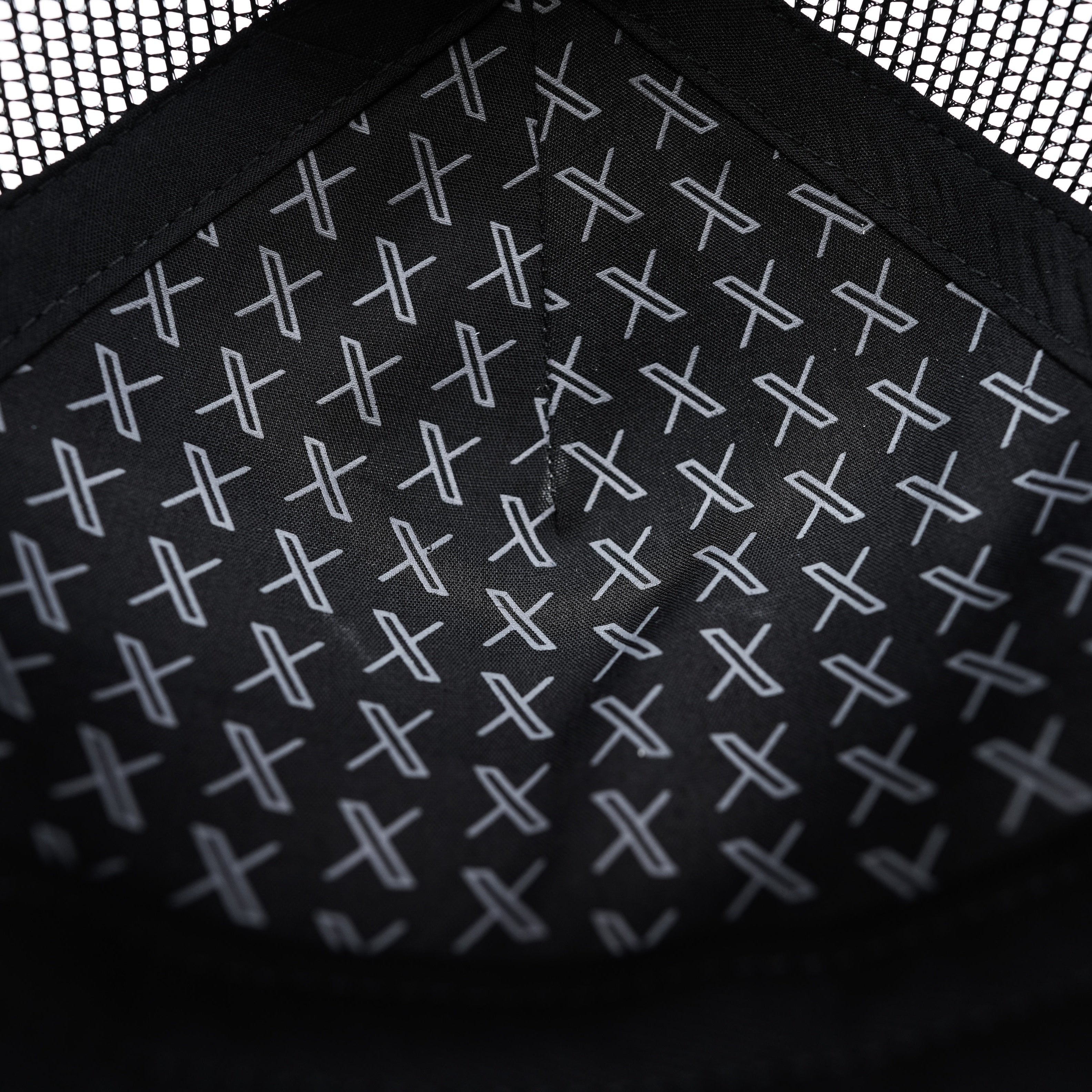 A closely cropped image of the Unisex 3D Logo Trucker Hat showing a pattern of X logos printed in white on the inside fabric of the black hat.